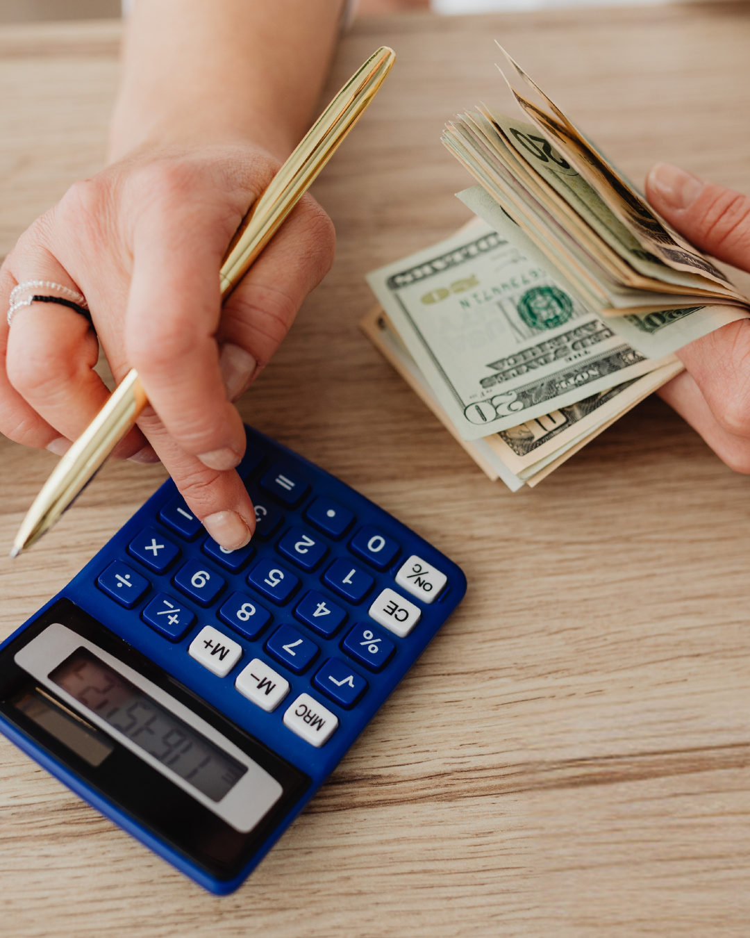Person typing on a calculator and holding money in their hand